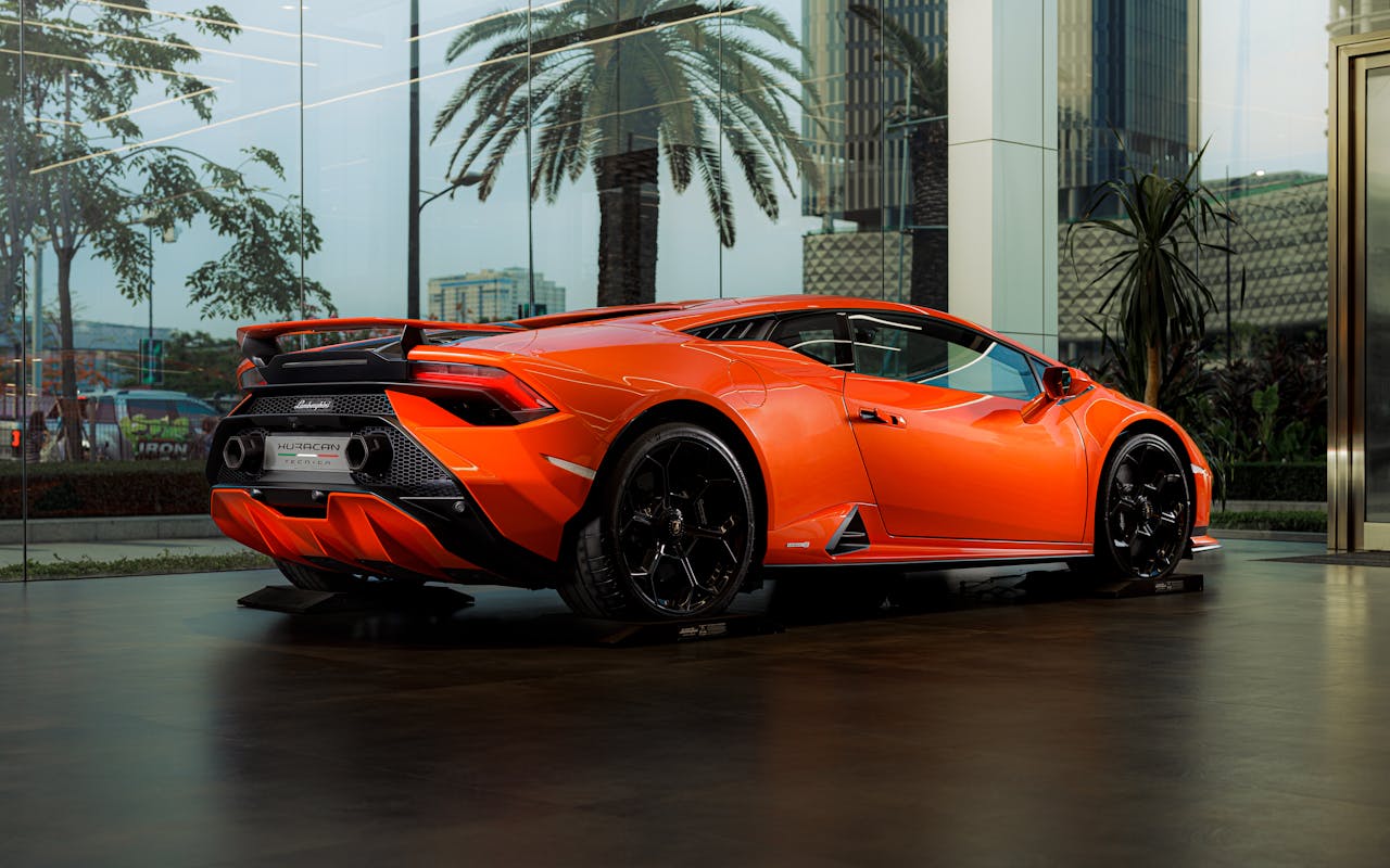 Bright orange sports car displayed in a sleek, modern dealership setting with cityscape in the background.