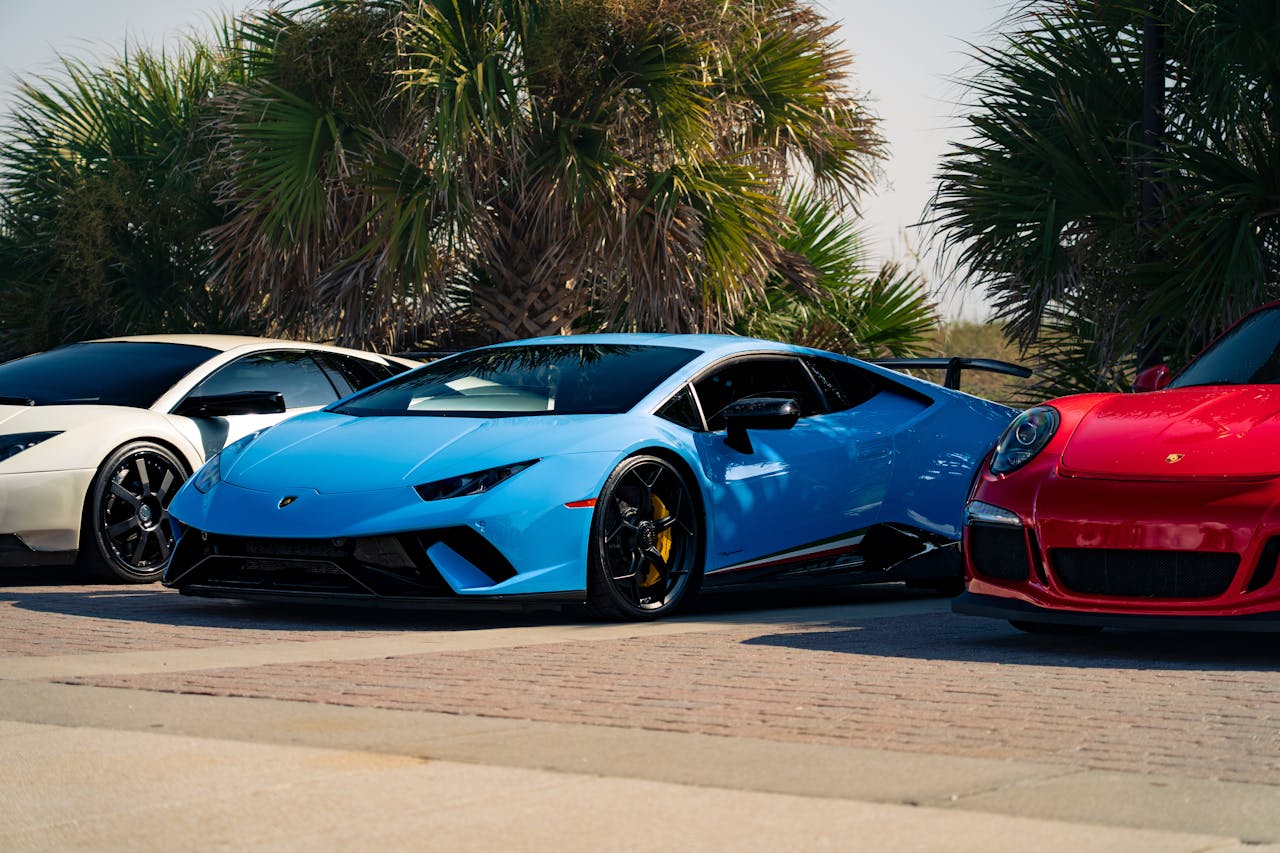 High-end sports cars parked among palm trees, showcasing sleek design and vibrant colors.